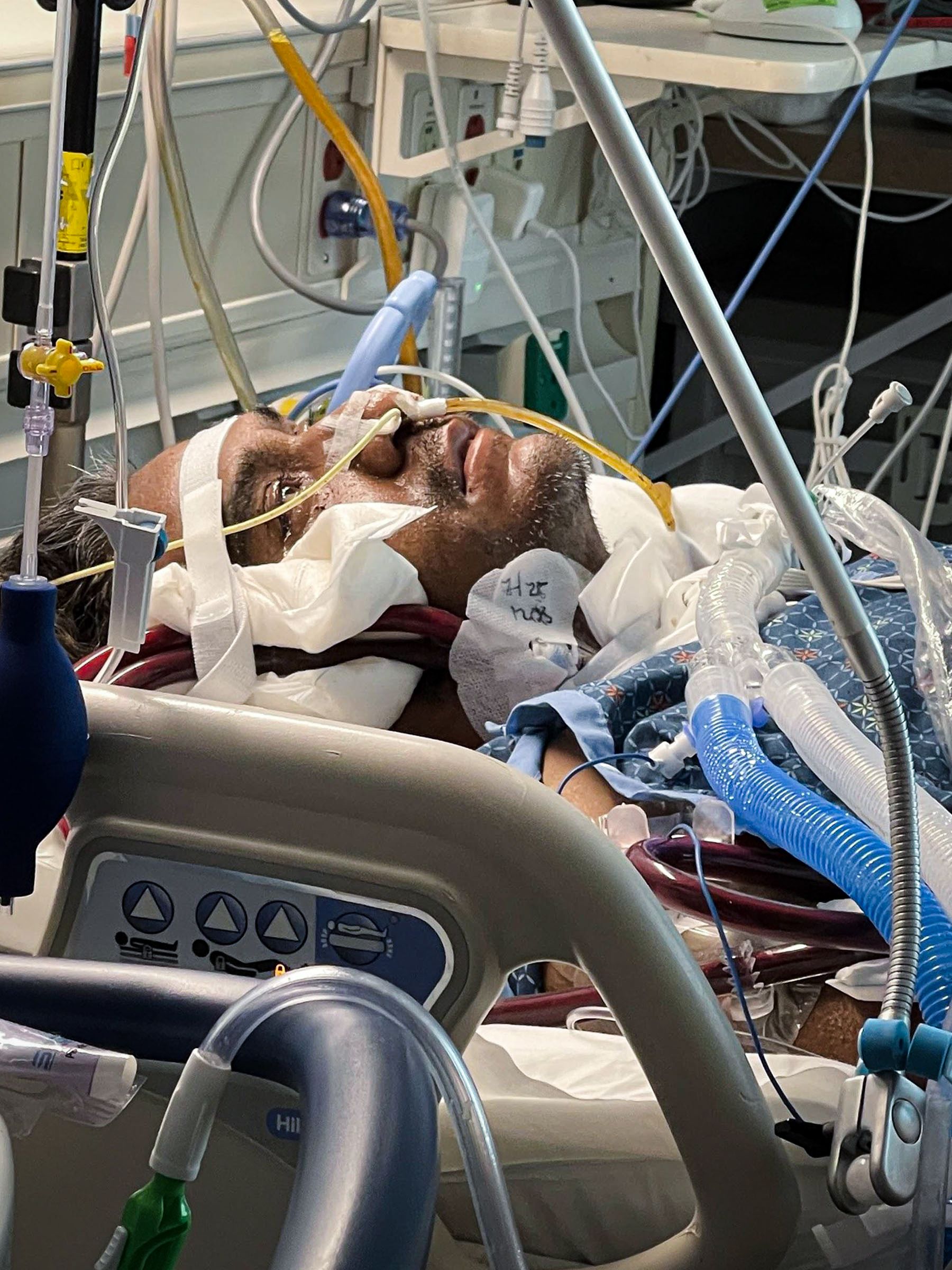 Manny in bed gazing sightlessly at the ceiling, surrounded by tubes and machines.