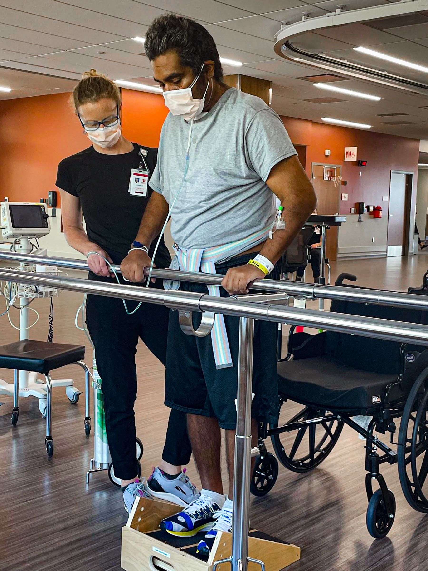 Shannon Wells stands to one side watching Manny strengthening his calves while holding onto an exercise bar.