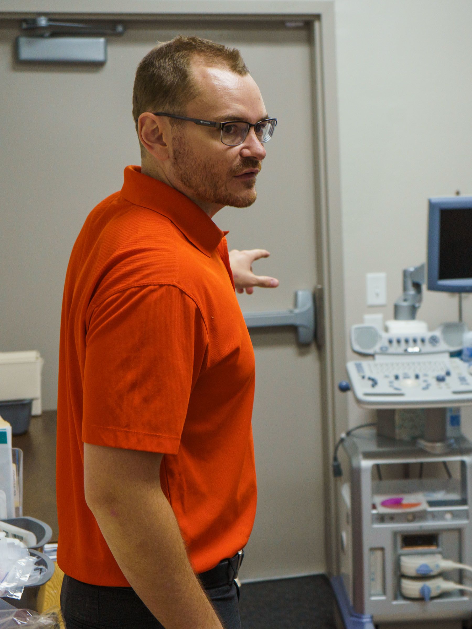 In an orange polo shirt, Hunter Adams points to an exit door in the Creek Valley Health Clinic.