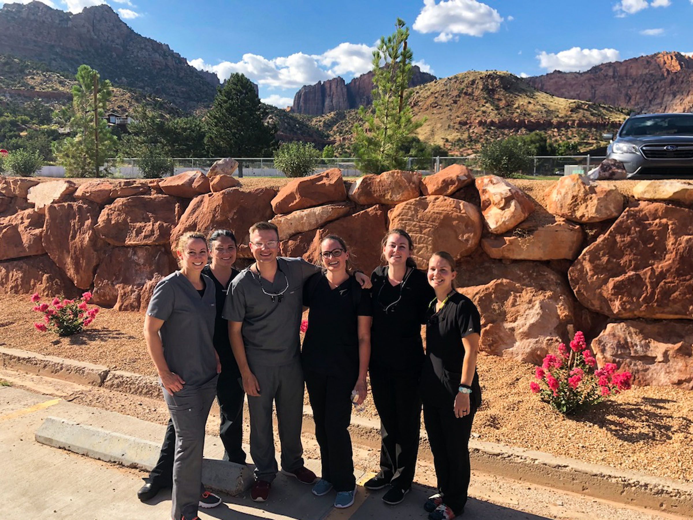 Dental students and Dental school staff in grey and black tunics, standing before red rock boulders.