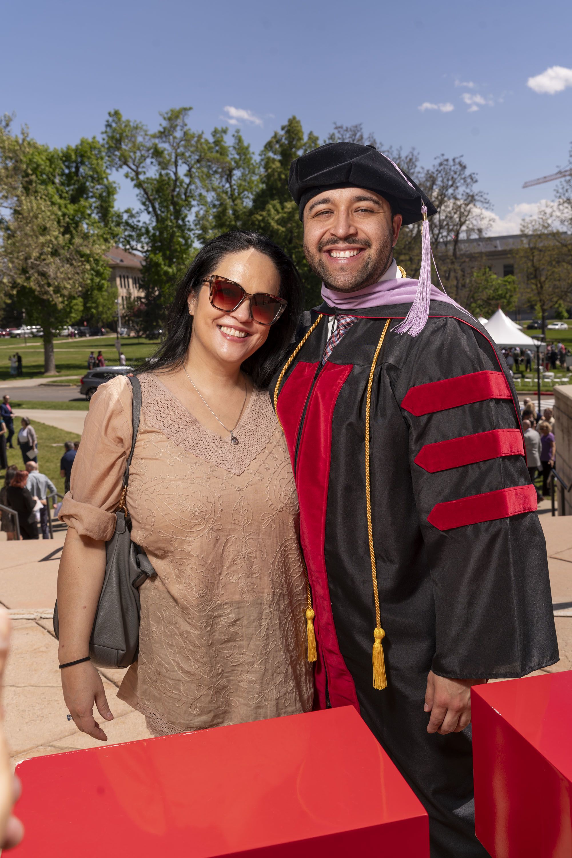 In a summer dress and sunglasses, Starr Avray poses with her dentist Alex Rojas in beret and gown at his graduation.