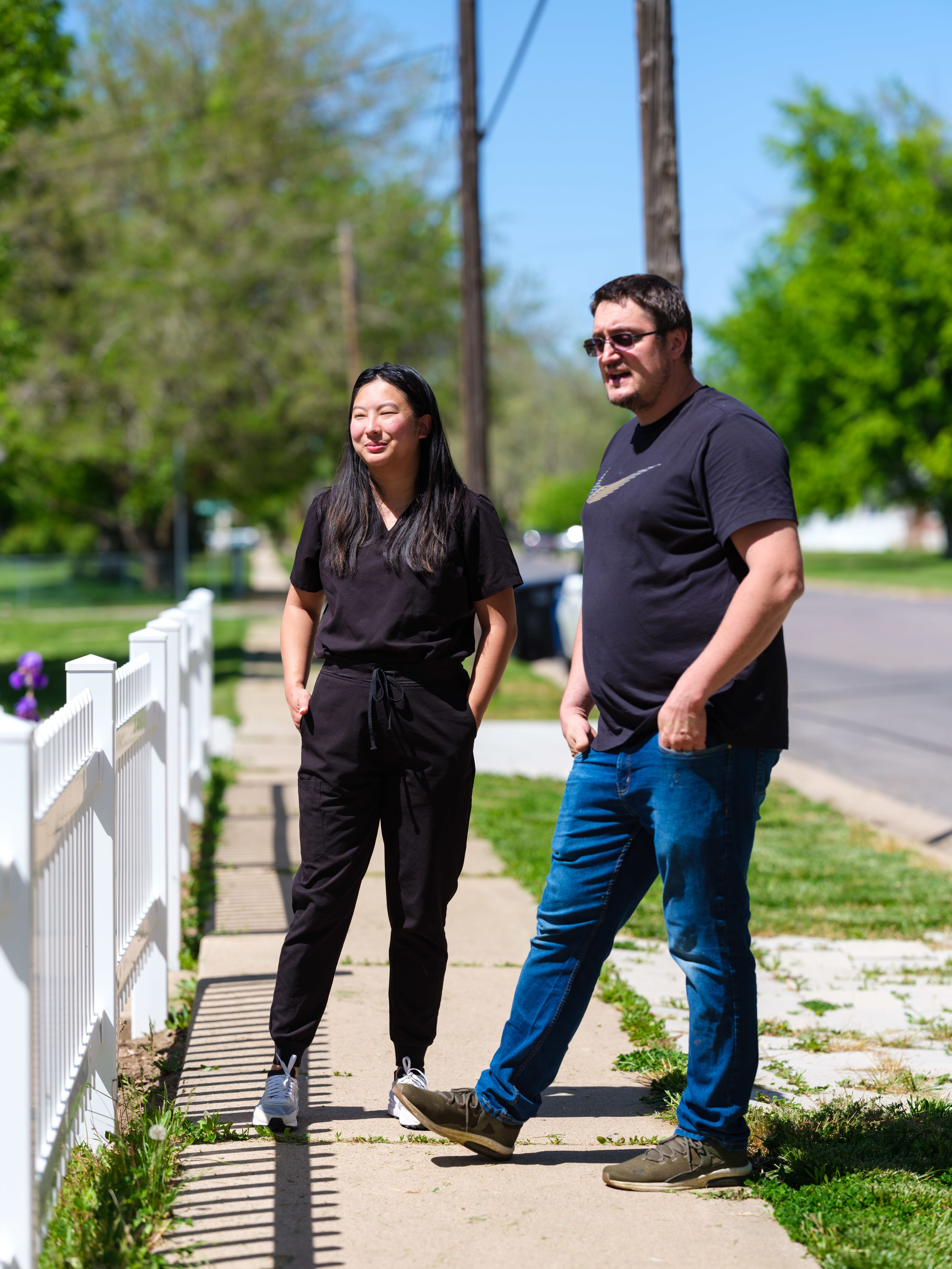 Ryann Lim with her UUSOD patient Sergii Ivanskii standing by a white picket fence in Farmington, Utah by Sergi's home. Above Lim stands with Sergii and his family and holds his youngest child. 